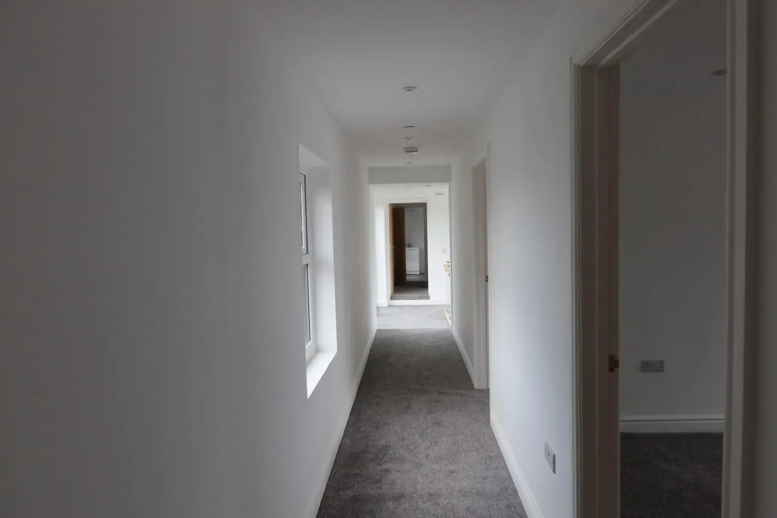 A long, newly renovated residential hallway with fresh white walls and grey carpet, showcasing the clean interior finish provided by Global Energy Insulation and Global Plastering