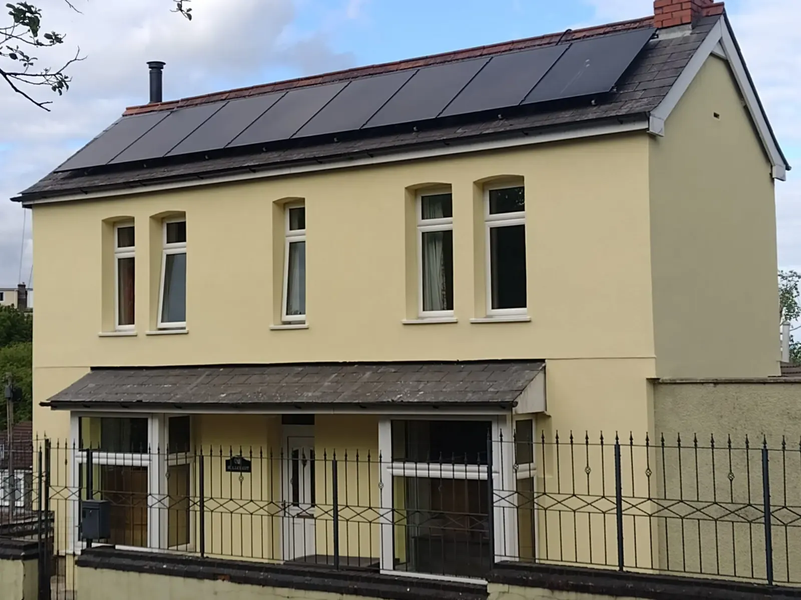 Detached house with pale yellow external wall insulation and rendering, plus solar panels.