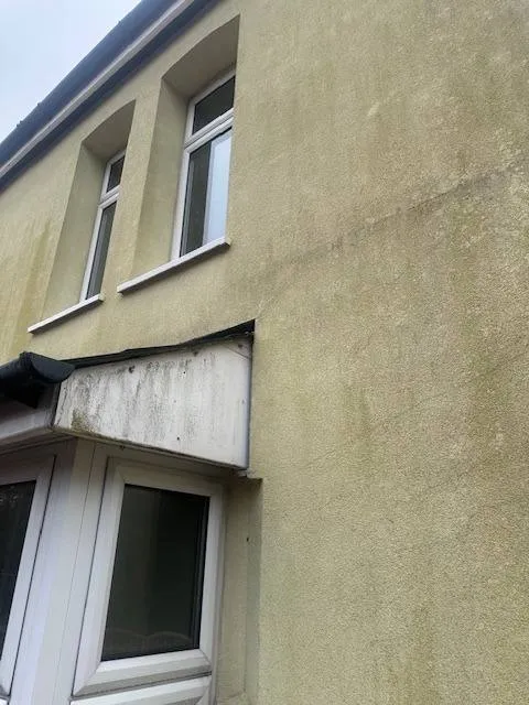 A close-up view of a house exterior featuring dirty, discoloured rendering prior to professional renovation or external wall insulation treatment