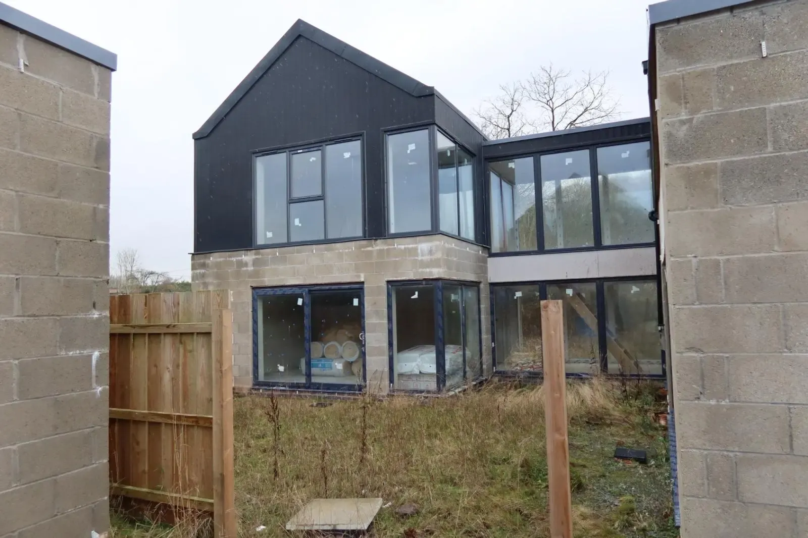A modern house under construction with exposed blockwork and rolls of insulation visible inside, preparing for thermal efficiency upgrades